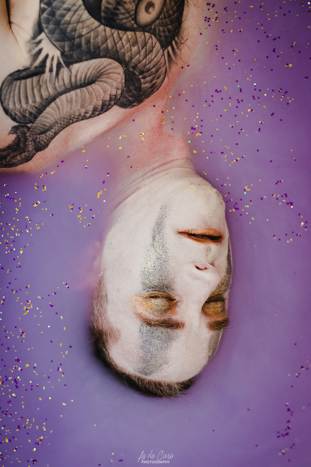 Portrait artistique d'un homme torse nu avec un tatouage et du maquillage sous de l'eau violette avec des paillettes à Grenoble
