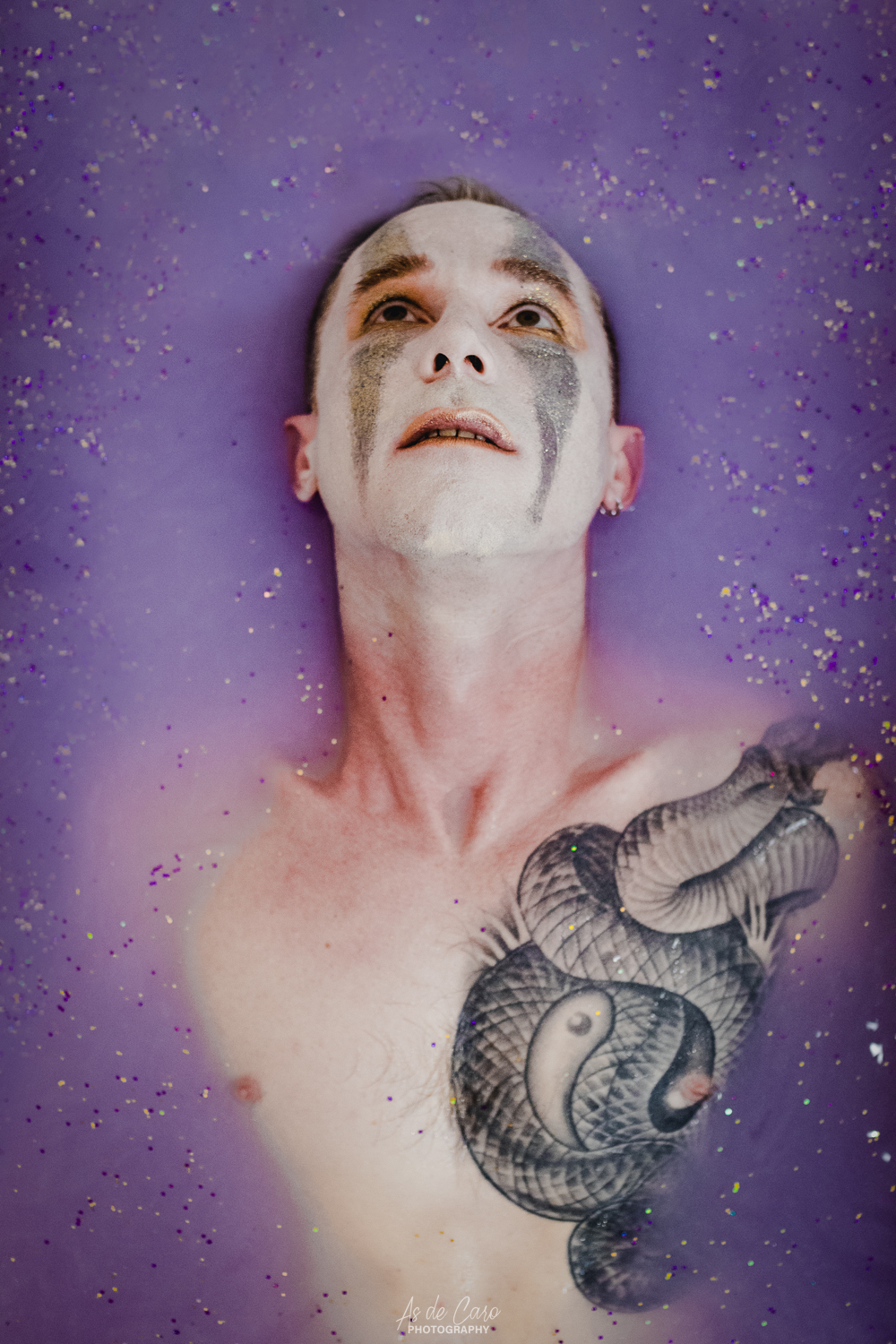 Portrait artistique d'un homme torse nu avec un tatouage et du maquillage sous de l'eau violette avec des paillettes à Grenoble